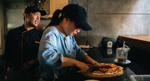 Restaurant worker cutting pizza.