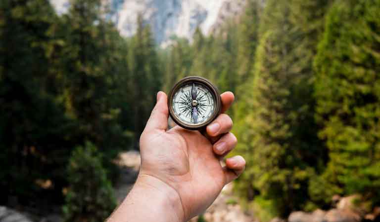 Hand holding a compass, while looking at mountains ahead.