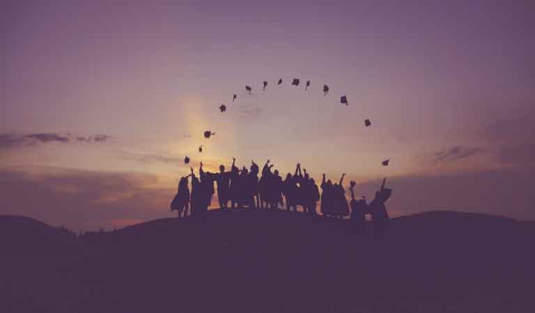 Graduates throwing their hats in the air at sunset.